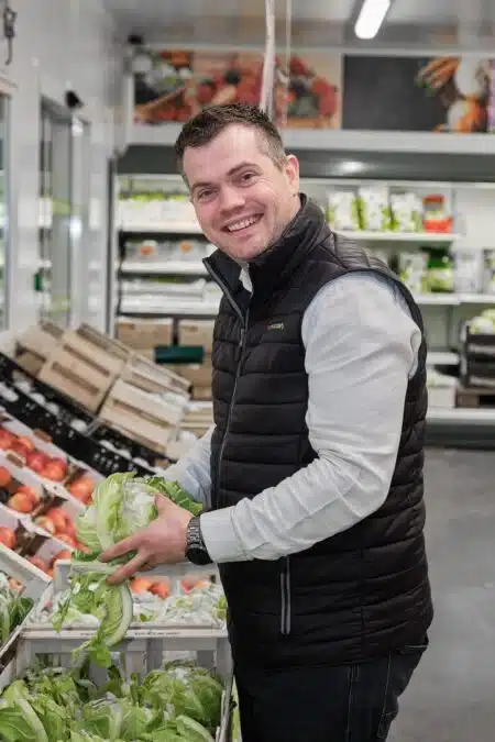 Collaborateur souriant, en train de ranger des salades dans le rayons légumes